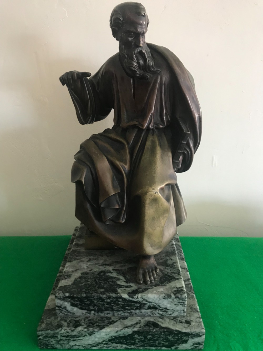 A patinated dark bronze sculpture depicting a draped, bearded ancient scholar seated on a green veined marble base.