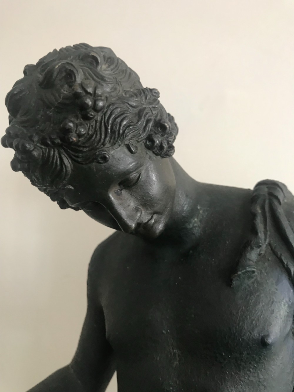 A dark patinated bronze sculpture depicting a standing nude male figure on a round stepped base. View II
