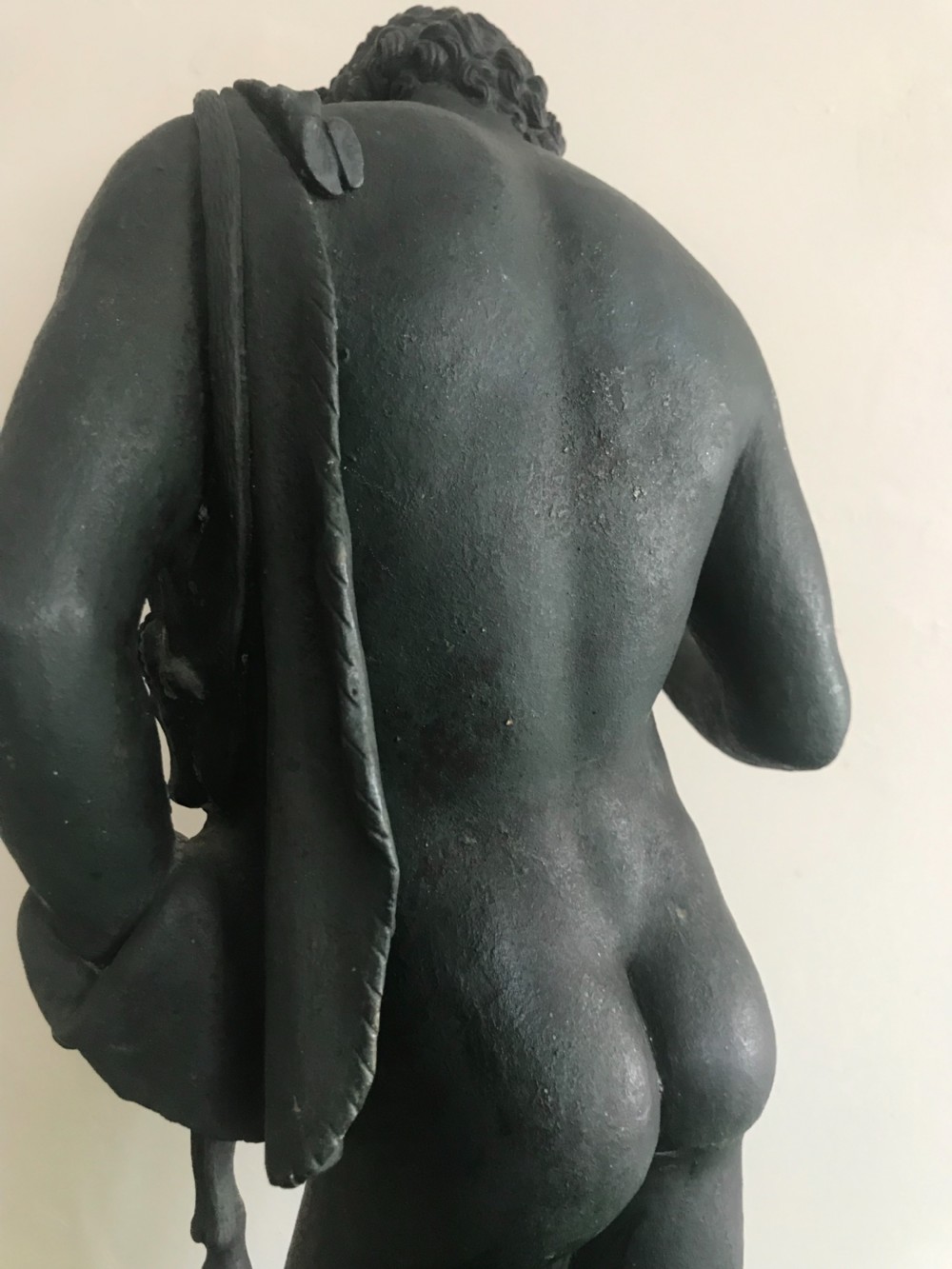 A dark patinated bronze sculpture depicting a standing nude male figure on a round stepped base. View IV