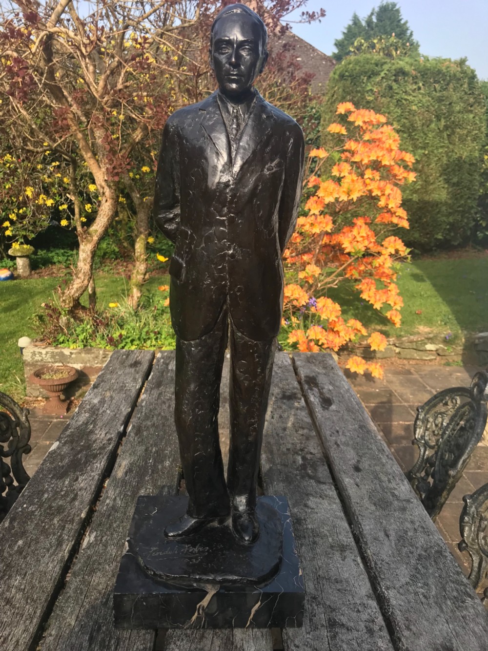 A dark patinated bronze statue depicting a standing man in a suit, mounted on a black marble base.