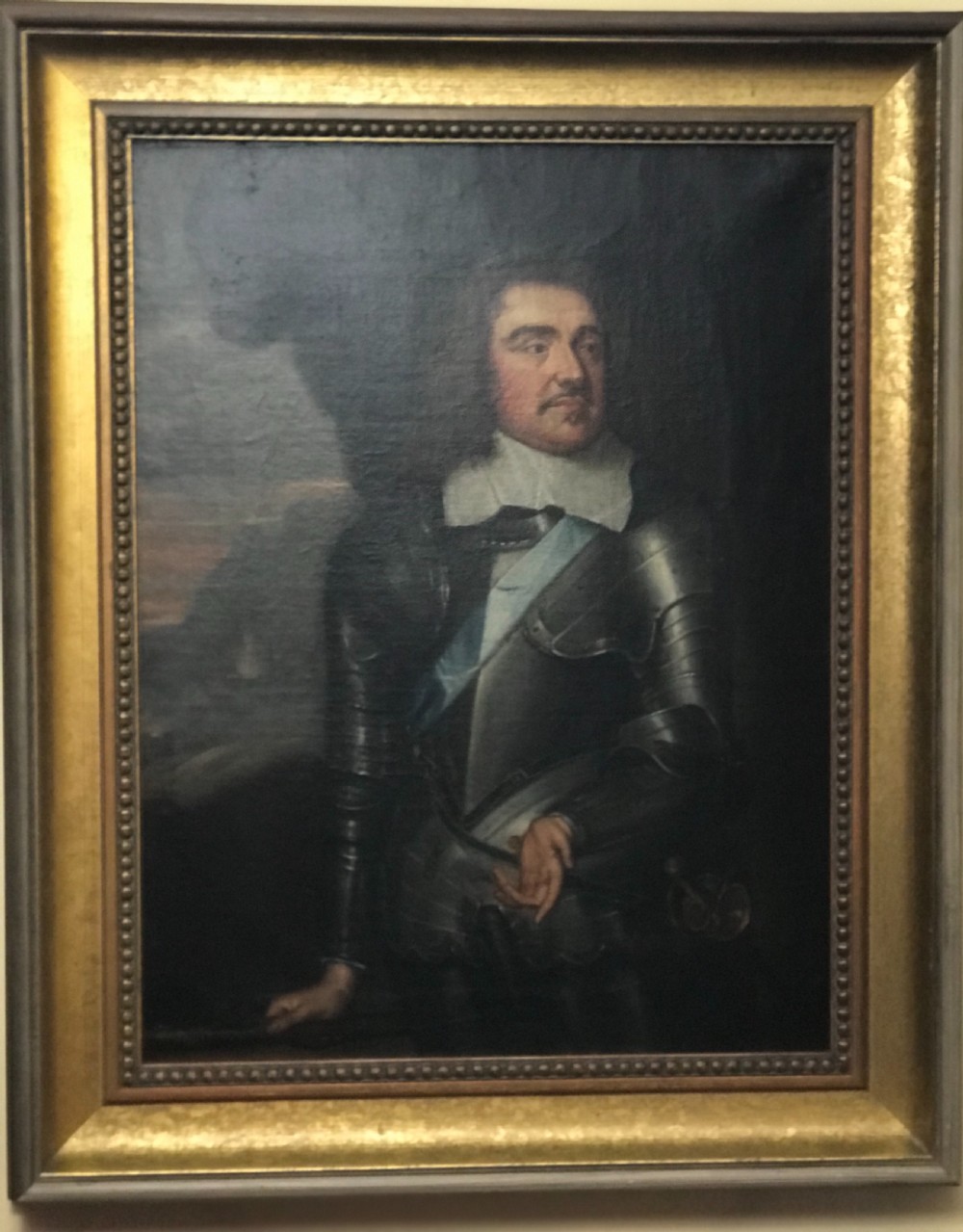 A seventeenth-century framed oil painting depicting a gentleman in plate armour with a white collar and blue sash against a dark background.