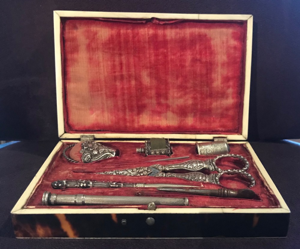 An open Victorian tortoiseshell rectangular sewing box featuring a crimson red velvet fitted interior with intricate silver tools including scissors and a thimble. View II