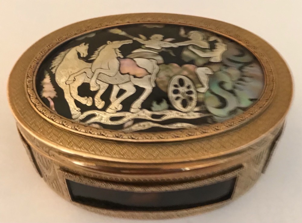 An oval gilt brass table snuff box featuring an inlaid mother-of-pearl lid panel depicting a chariot driven by horses.