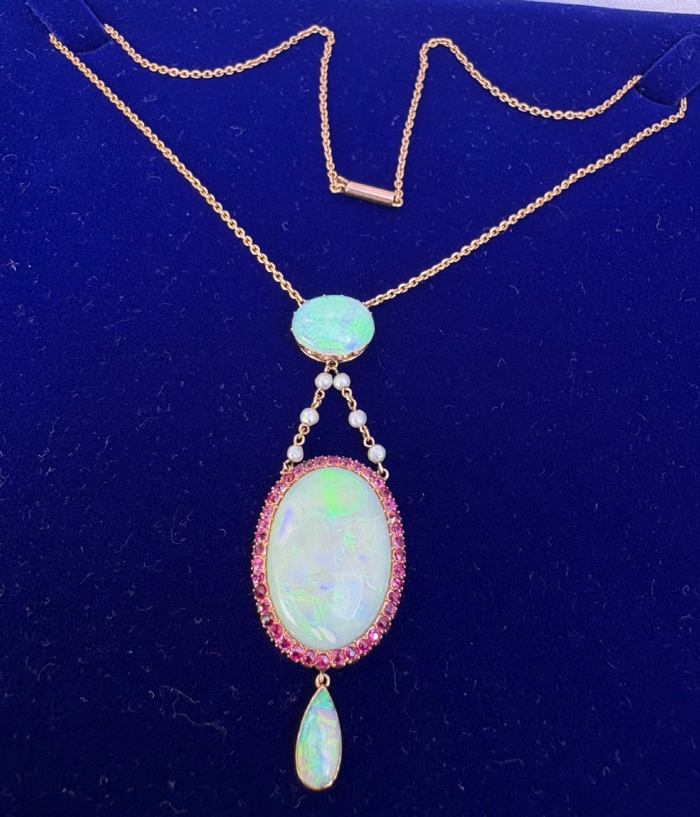 An antique Victorian 15ct yellow gold lavalier pendant set with two oval cabochon opals, a halo of rubies, and seed pearl connectors. View II