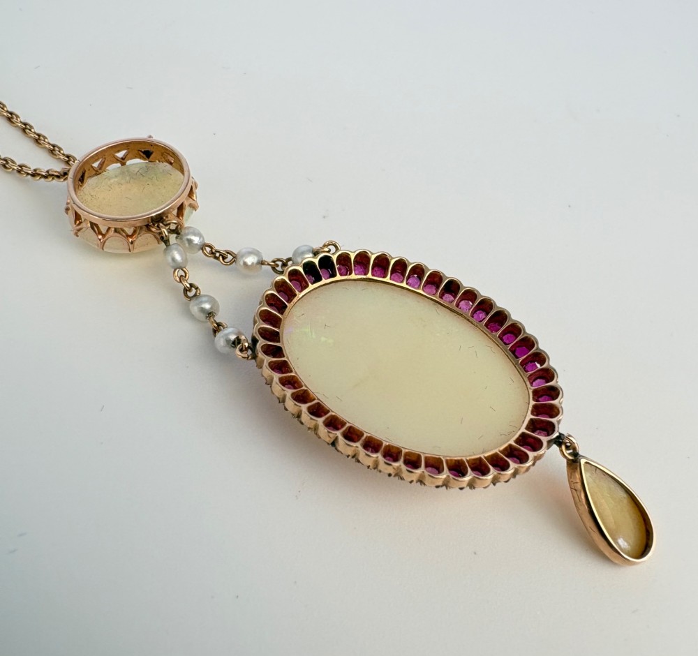 An antique Victorian 15ct yellow gold lavalier pendant set with two oval cabochon opals, a halo of rubies, and seed pearl connectors. View VIII
