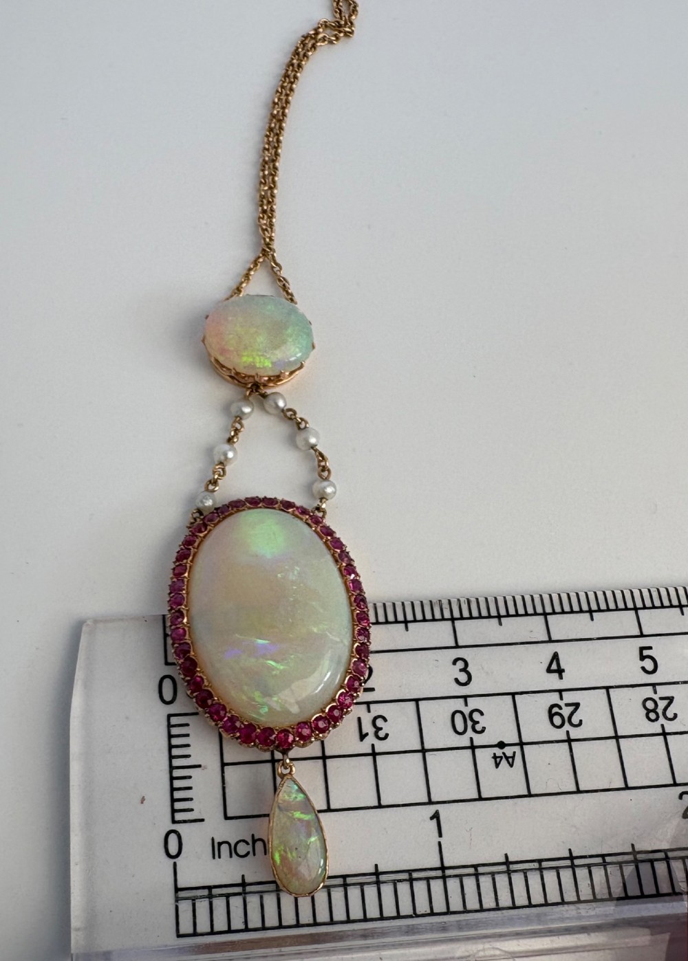 An antique Victorian 15ct yellow gold lavalier pendant set with two oval cabochon opals, a halo of rubies, and seed pearl connectors. View XI