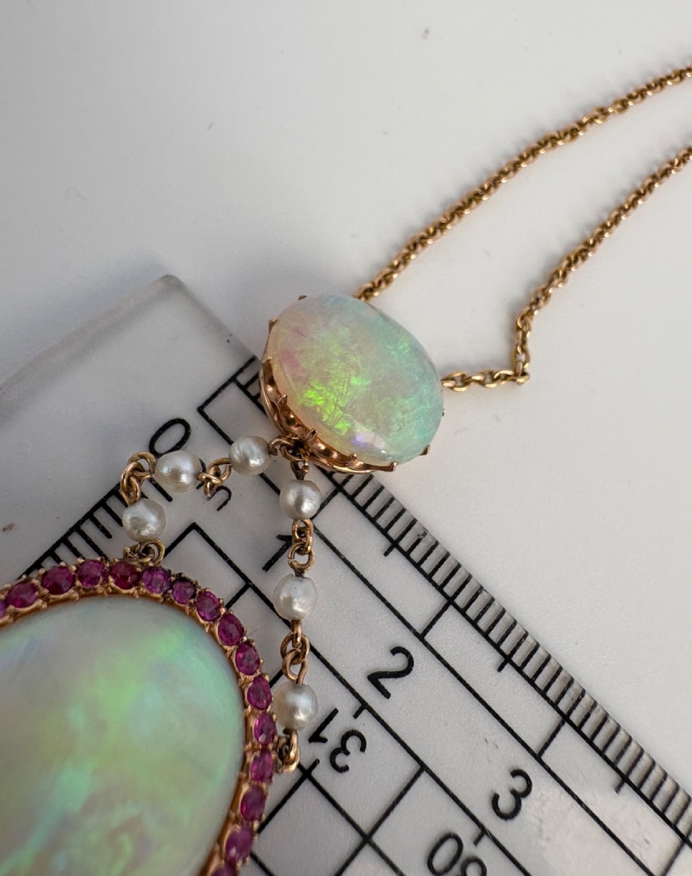 An antique Victorian 15ct yellow gold lavalier pendant set with two oval cabochon opals, a halo of rubies, and seed pearl connectors. View XIII