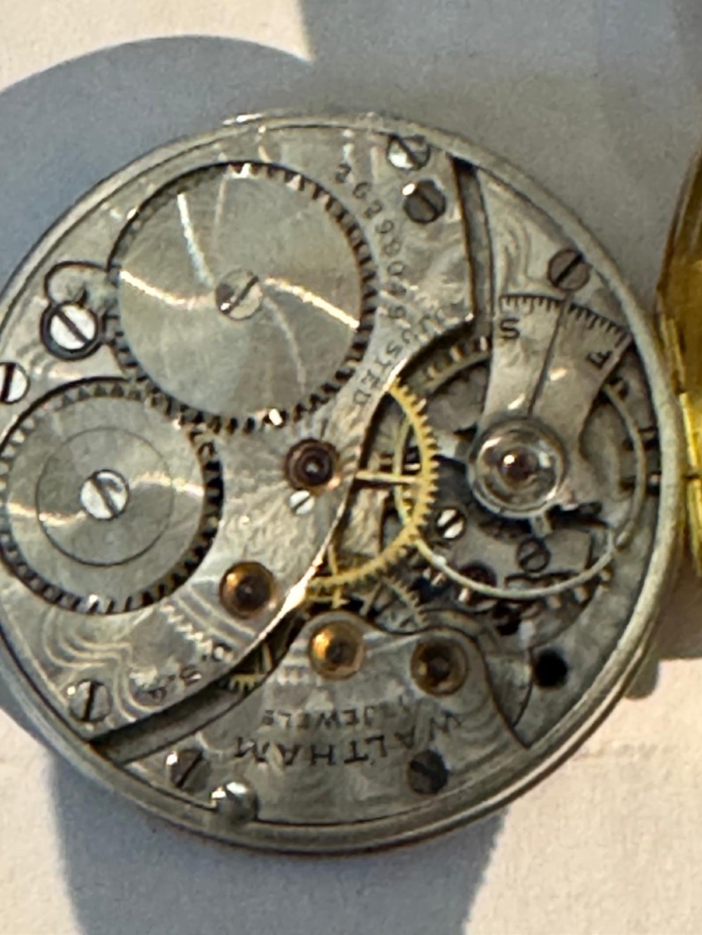 A 1920s 18ct gold Waltham wristwatch with a white enamel dial, black Arabic numerals, a red 12 marker, and a black woven strap. View V