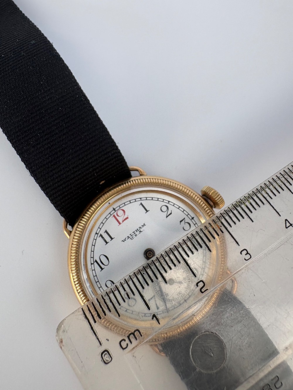 A 1920s 18ct gold Waltham wristwatch with a white enamel dial, black Arabic numerals, a red 12 marker, and a black woven strap. View VIII