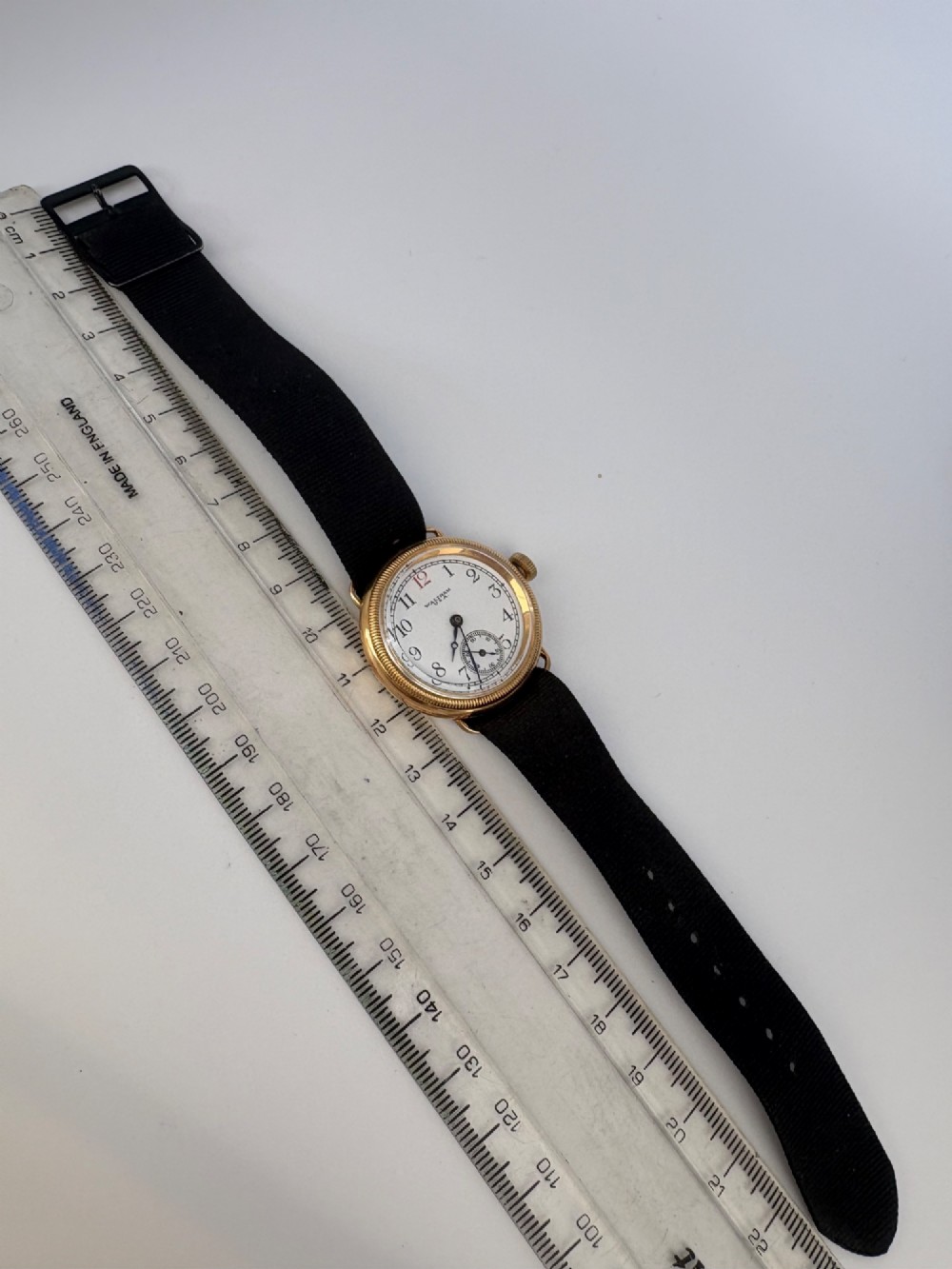 A 1920s 18ct gold Waltham wristwatch with a white enamel dial, black Arabic numerals, a red 12 marker, and a black woven strap. View IX