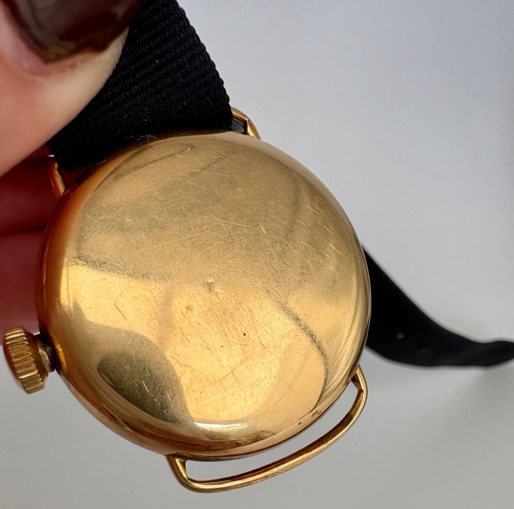A 1920s 18ct gold Waltham wristwatch with a white enamel dial, black Arabic numerals, a red 12 marker, and a black woven strap. View XI