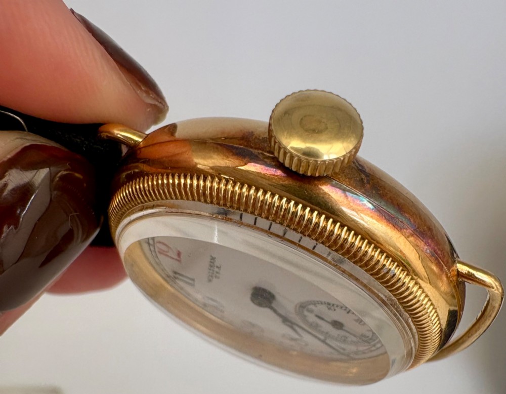 A 1920s 18ct gold Waltham wristwatch with a white enamel dial, black Arabic numerals, a red 12 marker, and a black woven strap. View XII