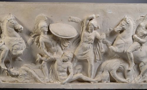 fig 1. A horizontal cream plaster bas-relief panel depicting a classical battle scene between cavalry warriors and shield-bearing soldiers.