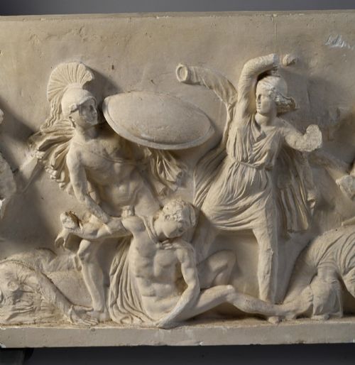 fig 2. A horizontal cream plaster bas-relief panel depicting a classical battle scene between cavalry warriors and shield-bearing soldiers.