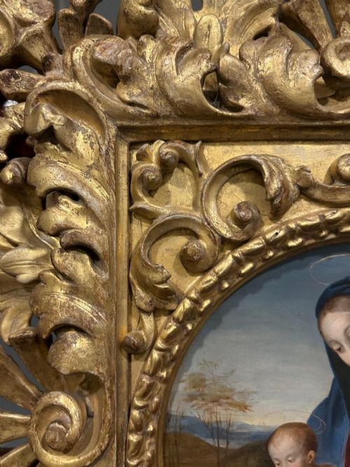 fig 3. A circular oil painting depicting the Virgin Mary in a blue cloak holding the Christ Child, enclosed within an ornate rectangular carved giltwood frame.
