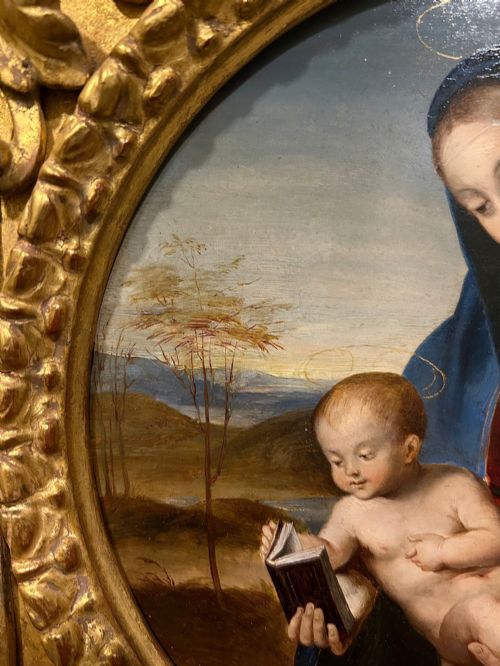 fig 4. A circular oil painting depicting the Virgin Mary in a blue cloak holding the Christ Child, enclosed within an ornate rectangular carved giltwood frame.
