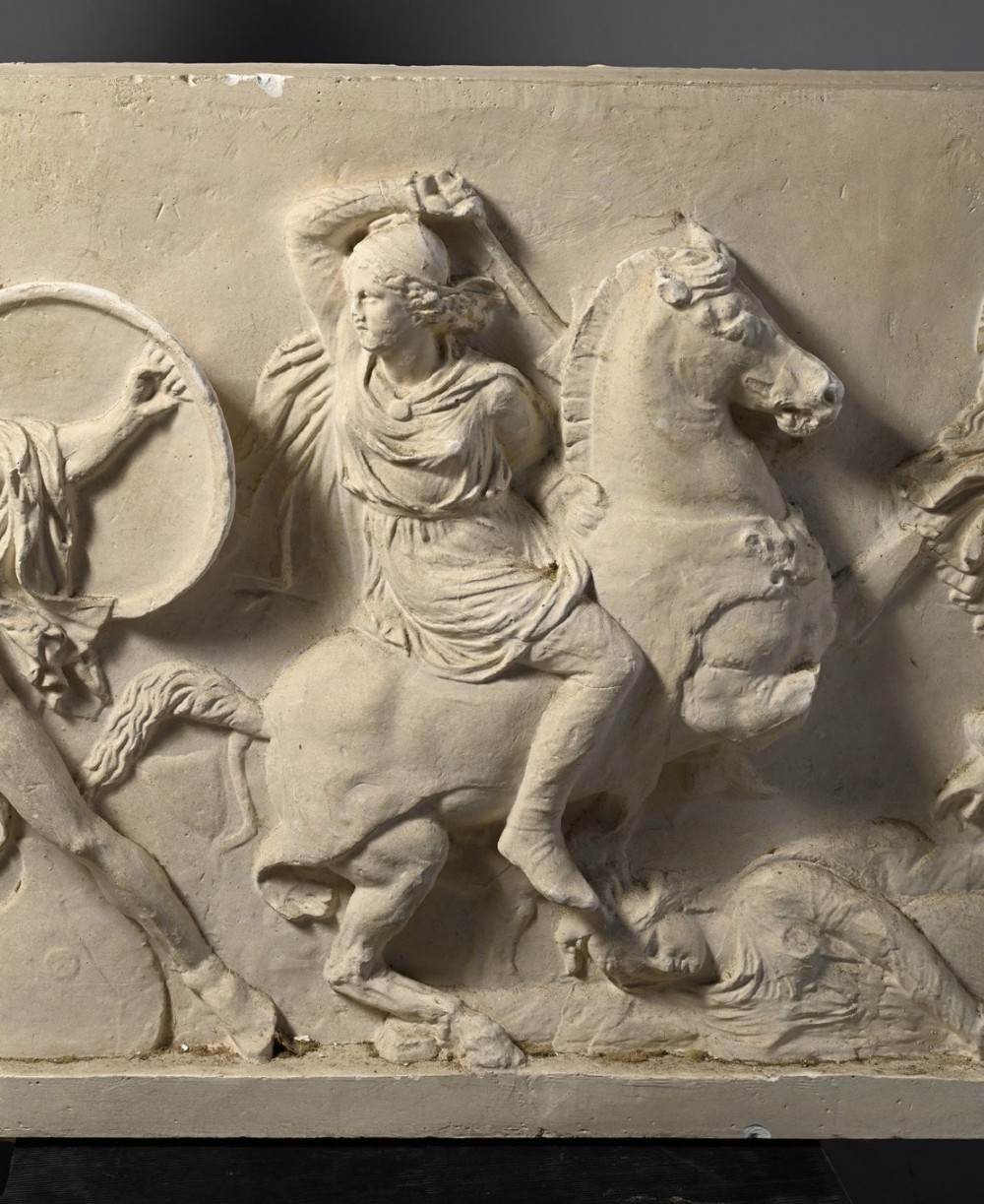 A horizontal cream plaster bas-relief panel depicting a classical battle scene between cavalry warriors and shield-bearing soldiers. View IV