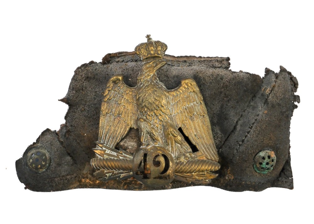 A framed shadow box displaying a stamped brass Napoleonic imperial eagle shako plate bearing the number 42 mounted on a distressed dark leather hat fragment. View II