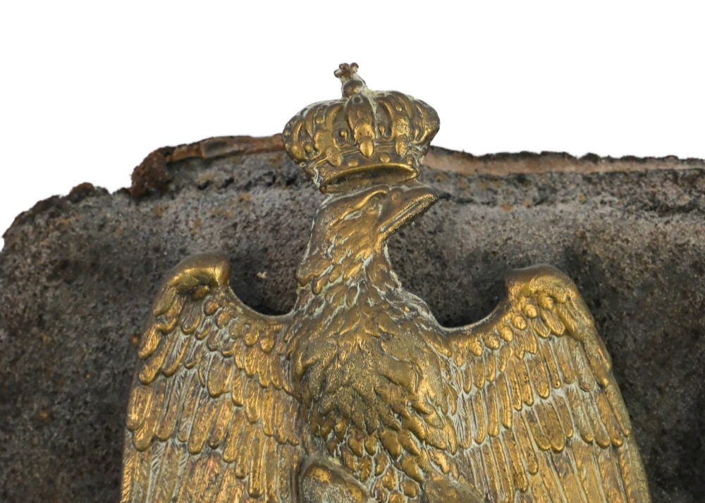 A framed shadow box displaying a stamped brass Napoleonic imperial eagle shako plate bearing the number 42 mounted on a distressed dark leather hat fragment. View III