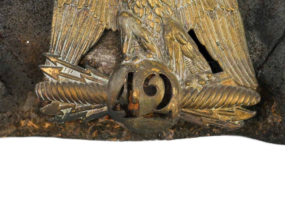 A framed shadow box displaying a stamped brass Napoleonic imperial eagle shako plate bearing the number 42 mounted on a distressed dark leather hat fragment. View IV