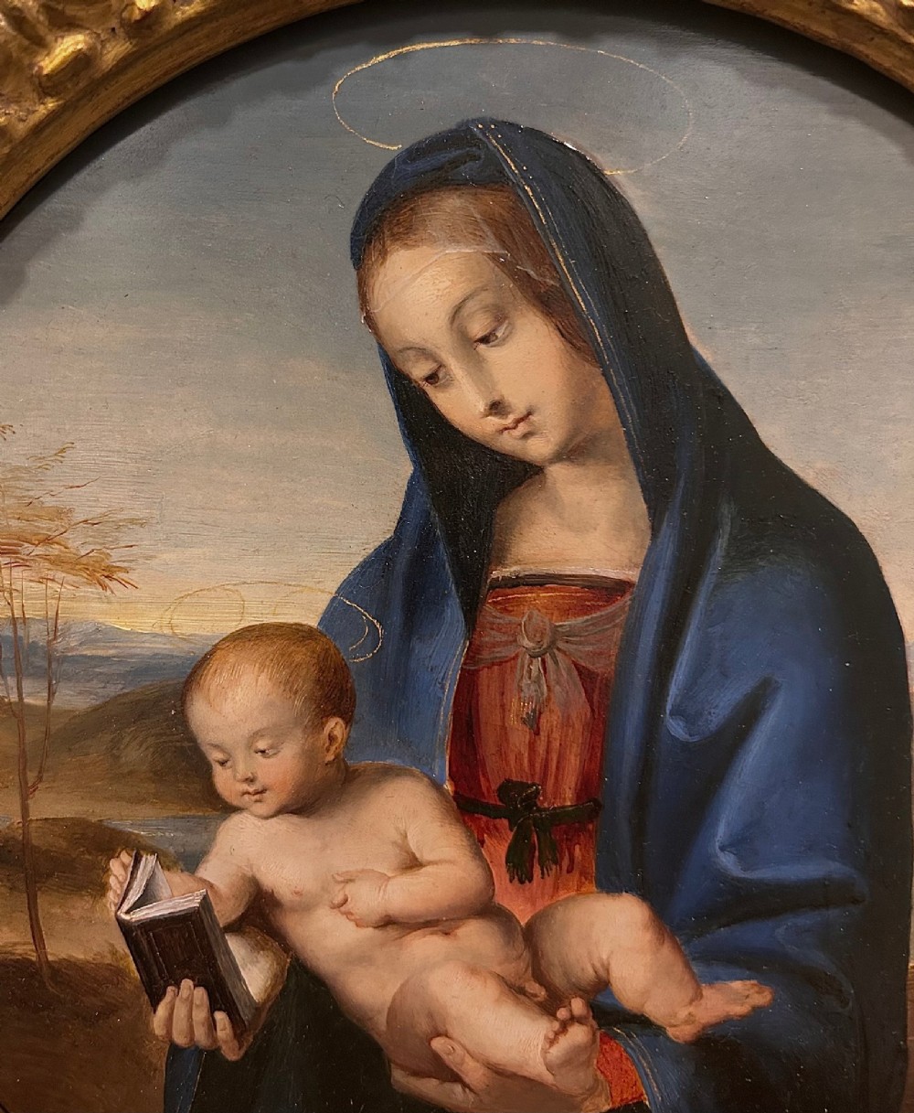 A circular oil painting depicting the Virgin Mary in a blue cloak holding the Christ Child, enclosed within an ornate rectangular carved giltwood frame. View VII