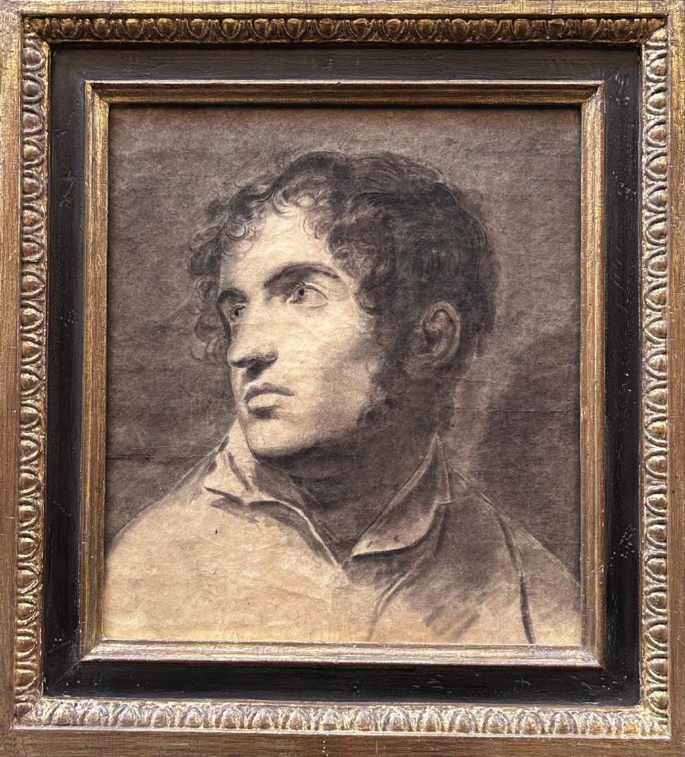 A framed monochrome charcoal drawing of a young man with curly hair facing left, enclosed in a moulded gilt and ebonised frame.