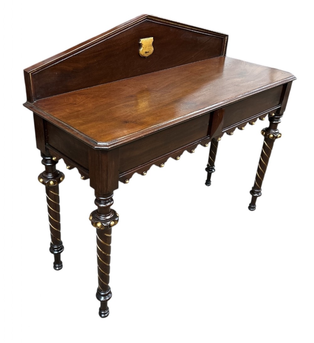A Victorian mahogany hall table featuring a raised backboard with a brass armorial shield plaque, barley twist turned legs with gilded accents, and a scalloped apron with brass bosses.