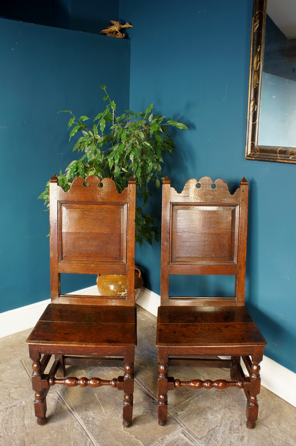 A pair of 17th-century dark oak Lancashire backstool chairs with panelled backs, shaped cresting rails, and turned front legs. View III