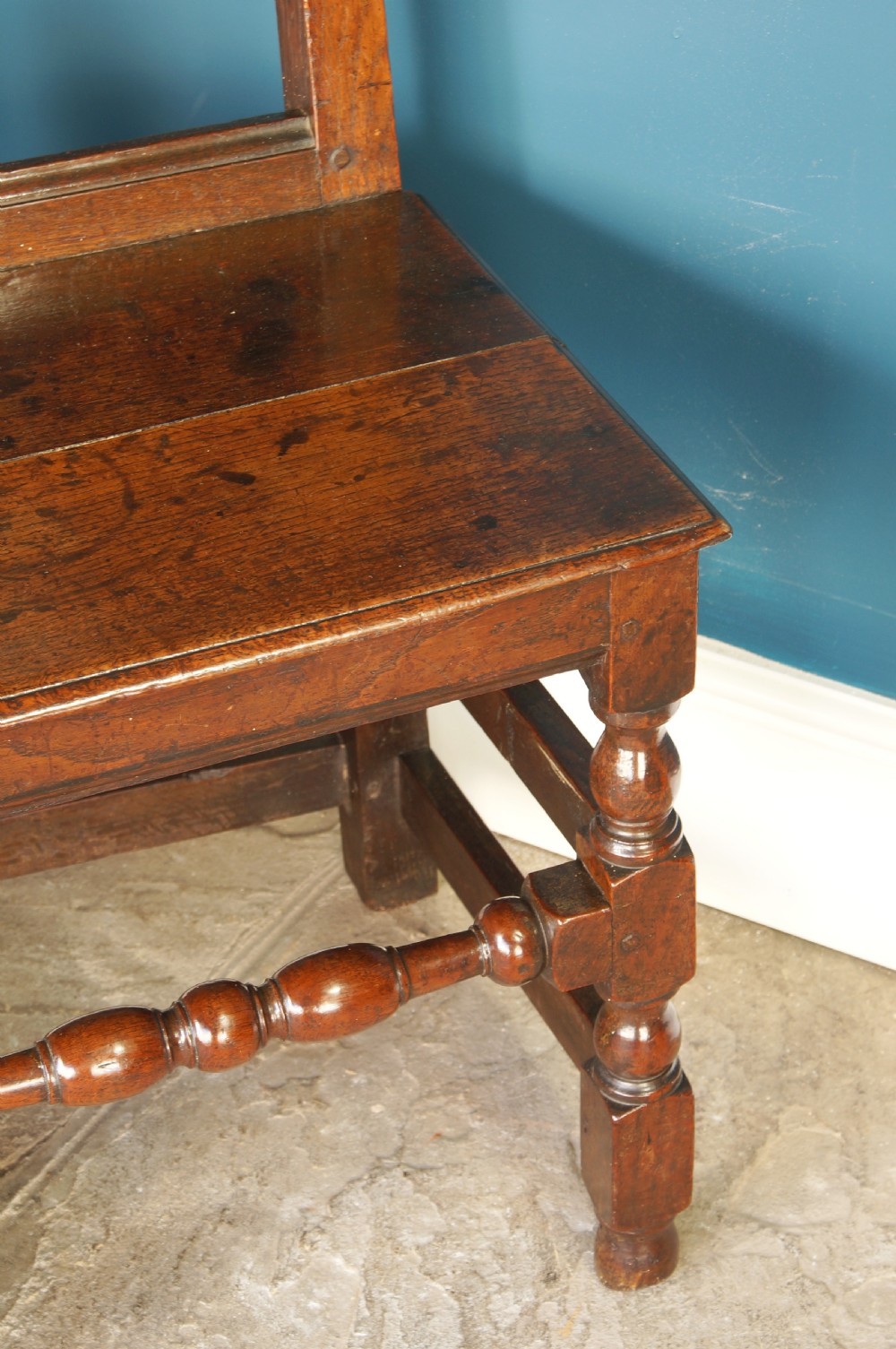 A pair of 17th-century dark oak Lancashire backstool chairs with panelled backs, shaped cresting rails, and turned front legs. View VII