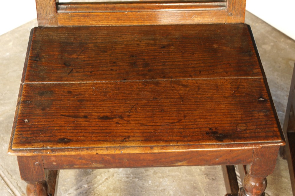A pair of 17th-century dark oak Lancashire backstool chairs with panelled backs, shaped cresting rails, and turned front legs. View VIII