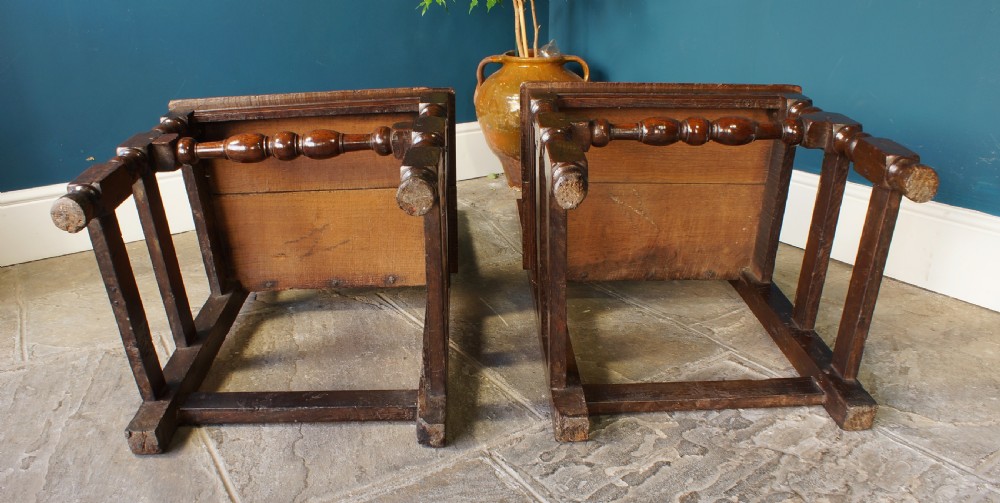 A pair of 17th-century dark oak Lancashire backstool chairs with panelled backs, shaped cresting rails, and turned front legs. View X