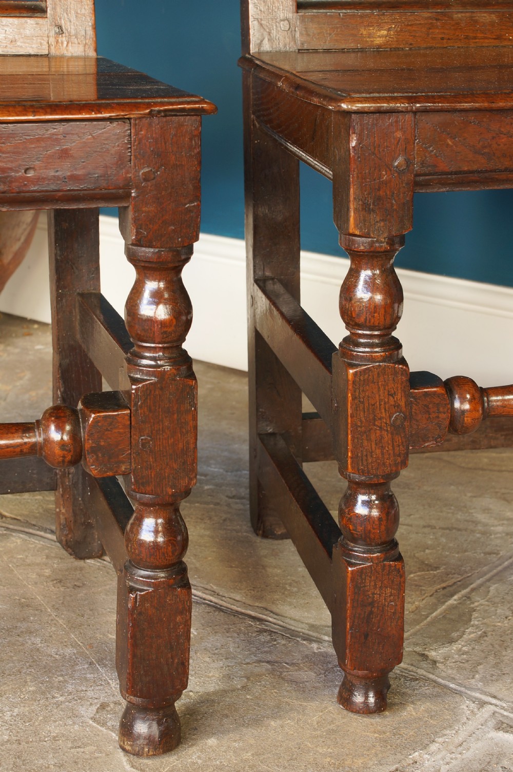 A pair of 17th-century dark oak Lancashire backstool chairs with panelled backs, shaped cresting rails, and turned front legs. View XII