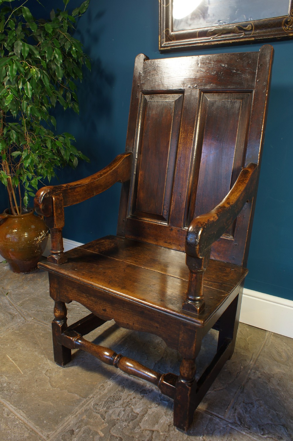An 18th century dark oak armchair featuring a double-panelled backrest, shaped open arms, and turned front legs connected by a stretcher. View II