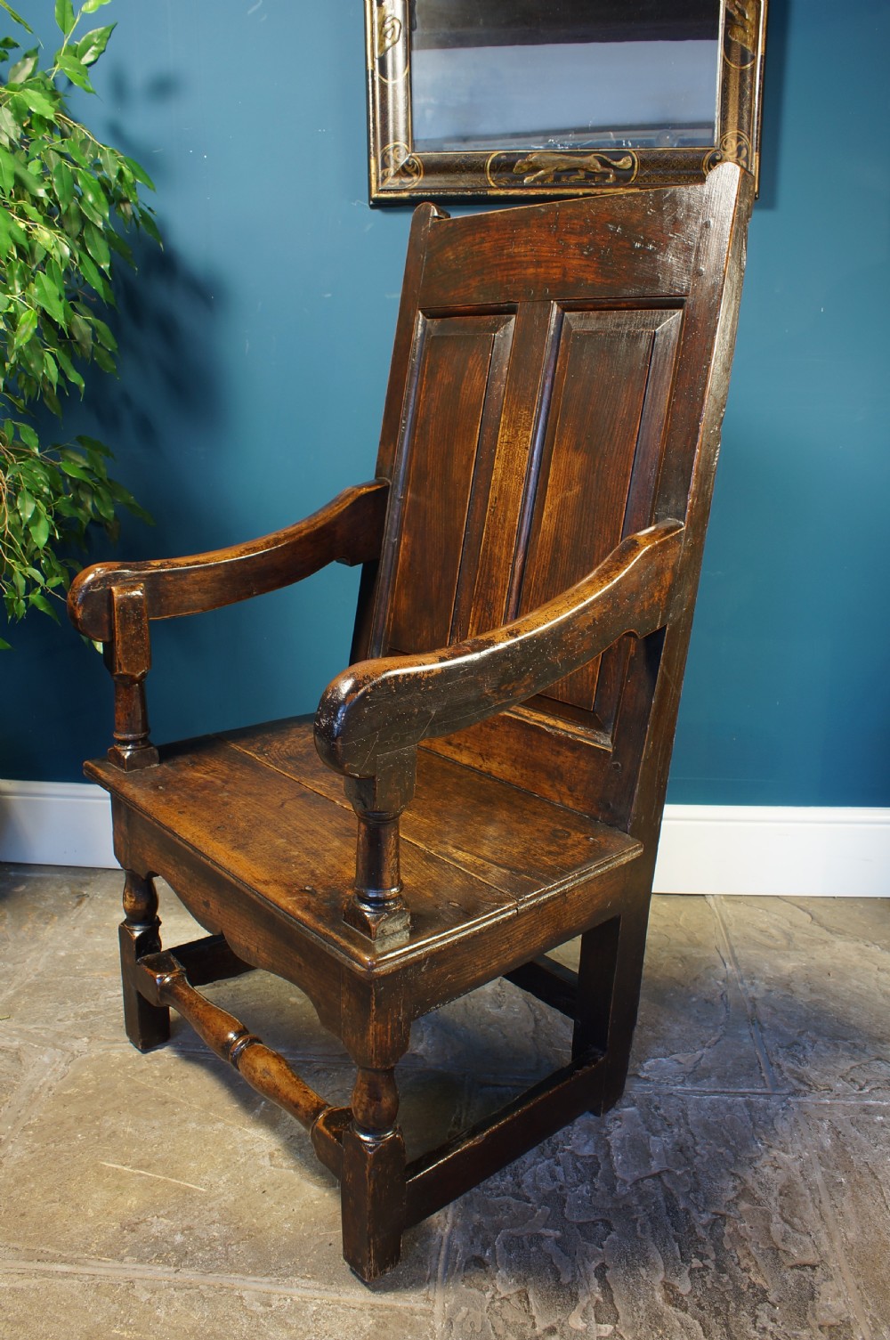 An 18th century dark oak armchair featuring a double-panelled backrest, shaped open arms, and turned front legs connected by a stretcher. View III