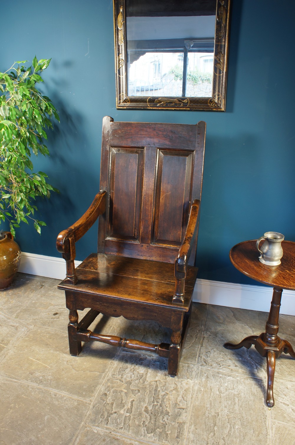 An 18th century dark oak armchair featuring a double-panelled backrest, shaped open arms, and turned front legs connected by a stretcher. View V