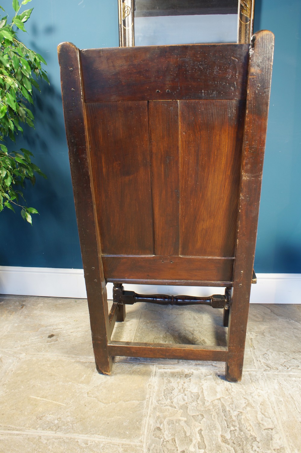 An 18th century dark oak armchair featuring a double-panelled backrest, shaped open arms, and turned front legs connected by a stretcher. View VI