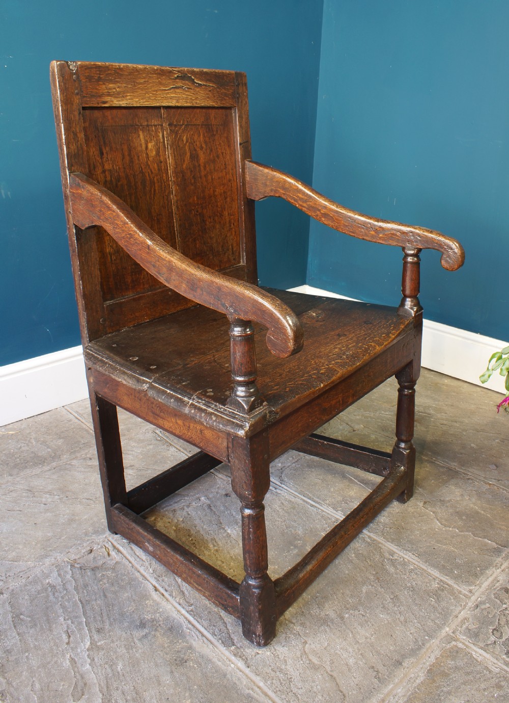 A 17th-century dark oak wainscot armchair featuring a solid panelled back, curved arms, turned front legs, and square stretchers. View III