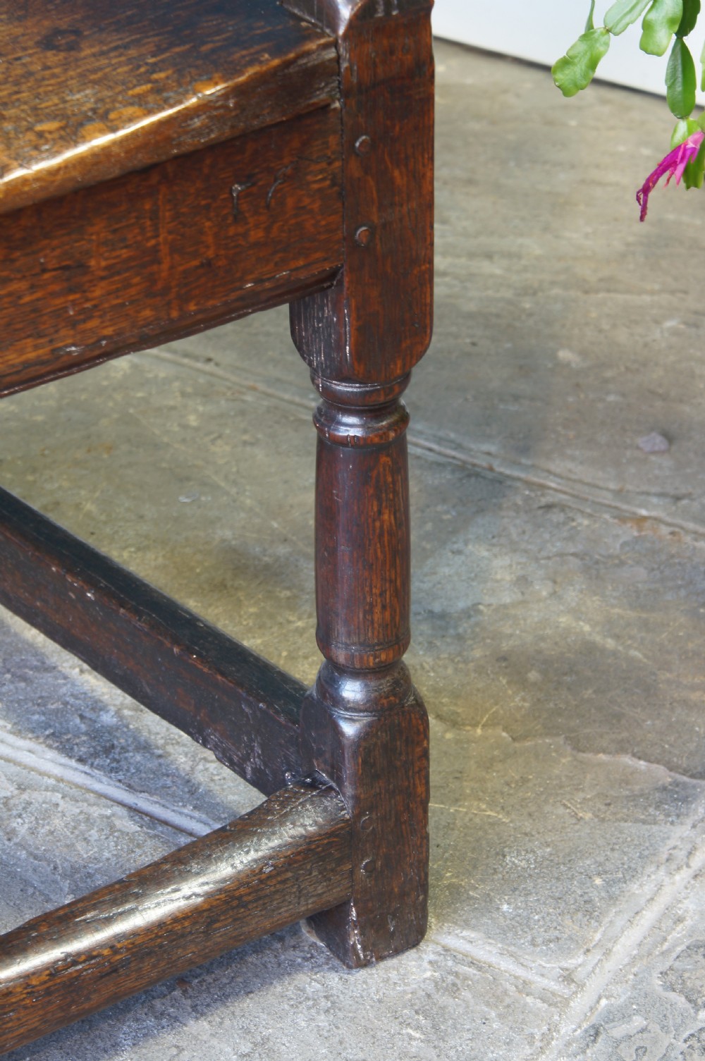 A 17th-century dark oak wainscot armchair featuring a solid panelled back, curved arms, turned front legs, and square stretchers. View V