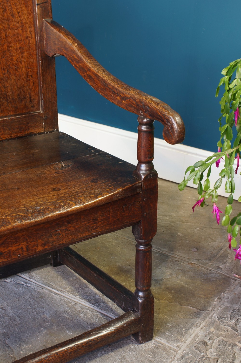A 17th-century dark oak wainscot armchair featuring a solid panelled back, curved arms, turned front legs, and square stretchers. View VI