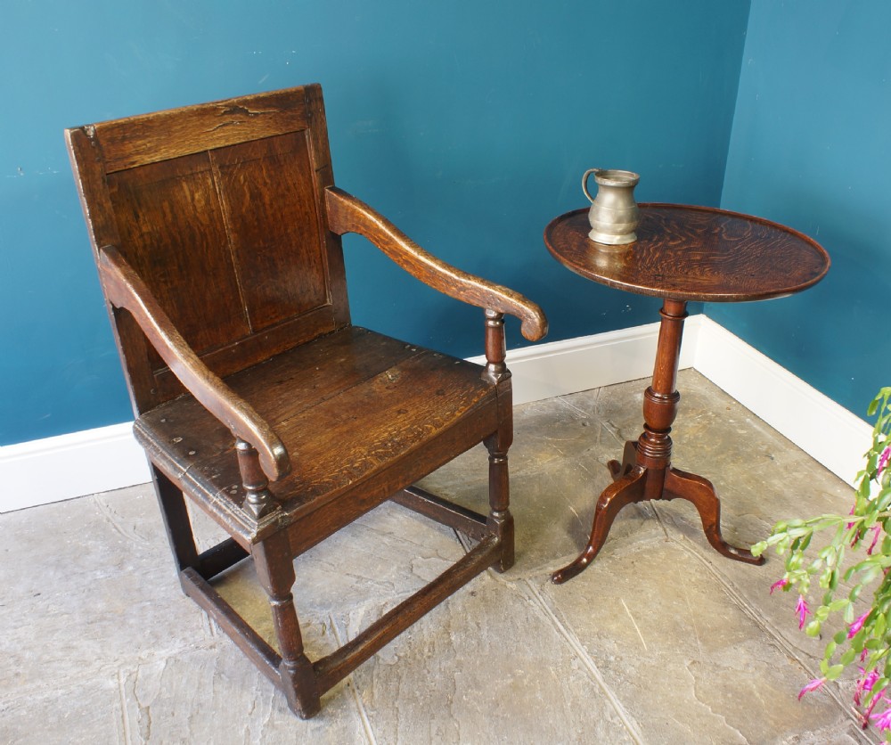 A 17th-century dark oak wainscot armchair featuring a solid panelled back, curved arms, turned front legs, and square stretchers. View VII