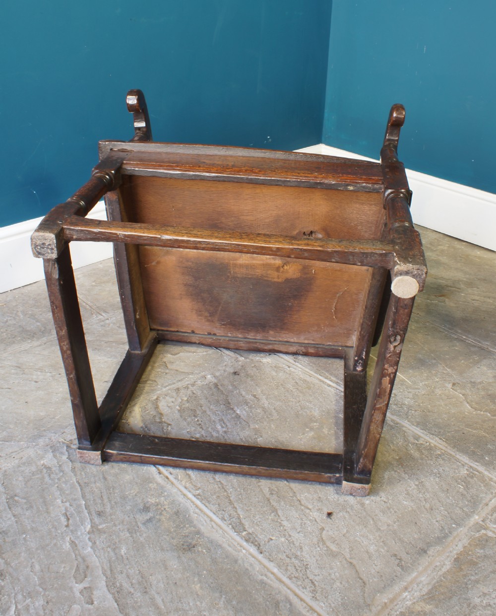 A 17th-century dark oak wainscot armchair featuring a solid panelled back, curved arms, turned front legs, and square stretchers. View IX