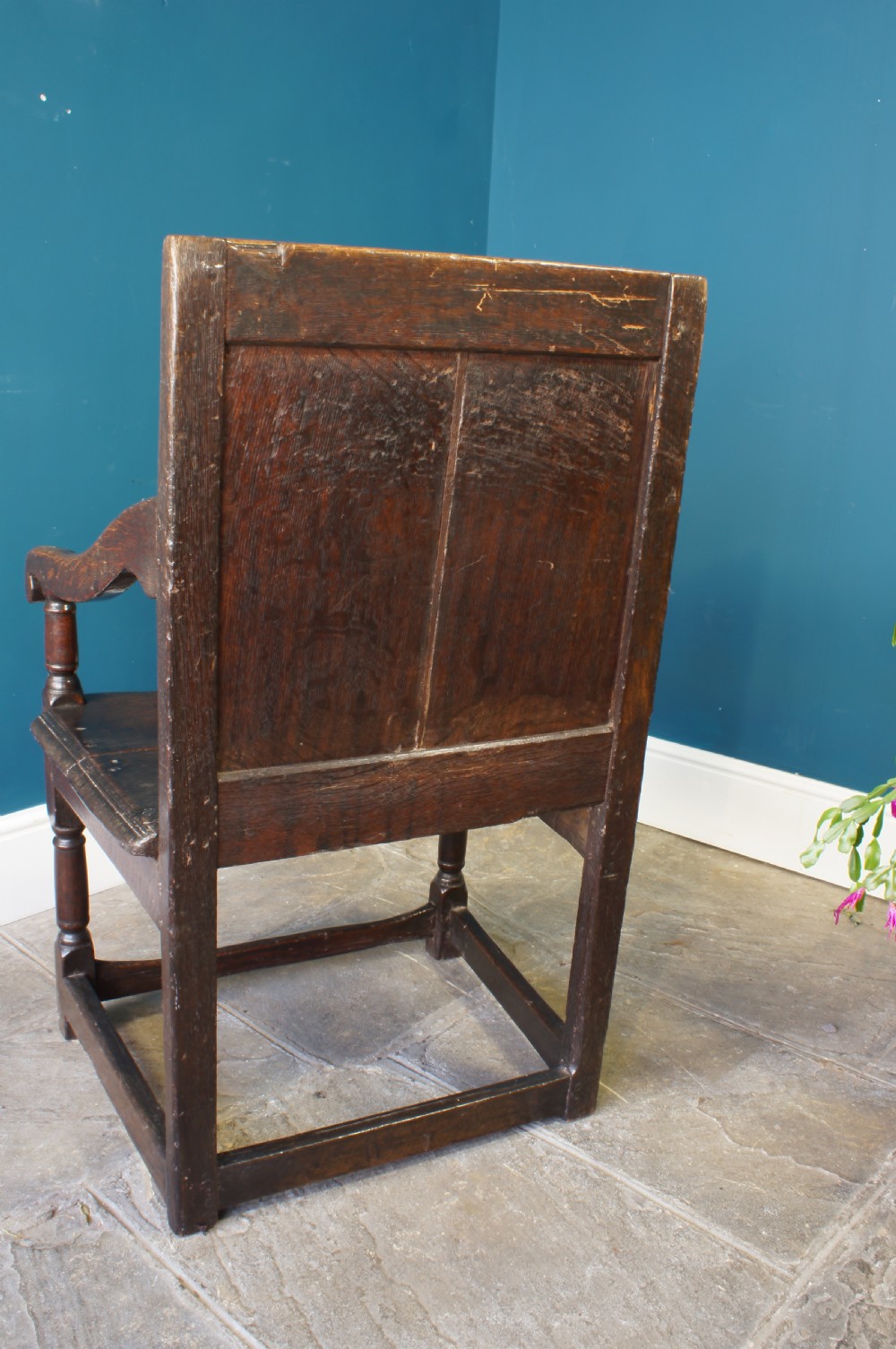 A 17th-century dark oak wainscot armchair featuring a solid panelled back, curved arms, turned front legs, and square stretchers. View X