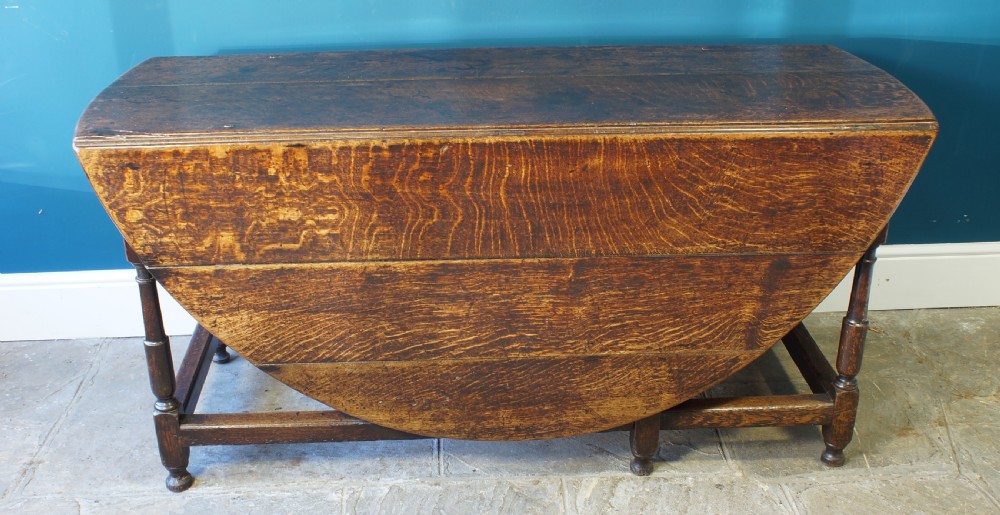A large 18th-century dark oak gateleg dining table with a circular drop-leaf top supported by turned legs and stretchers. View IX