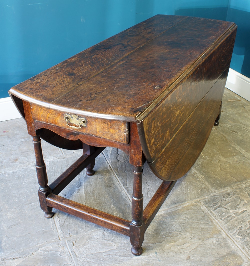 A large 18th-century dark oak gateleg dining table with a circular drop-leaf top supported by turned legs and stretchers. View V