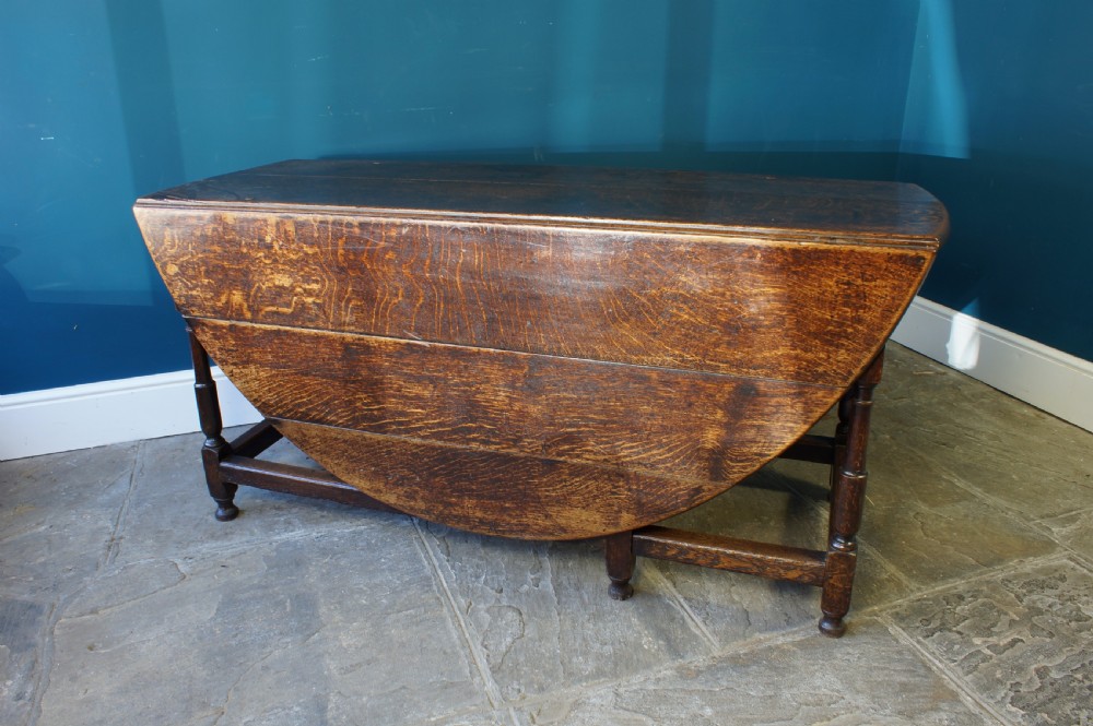 A large 18th-century dark oak gateleg dining table with a circular drop-leaf top supported by turned legs and stretchers. View VI
