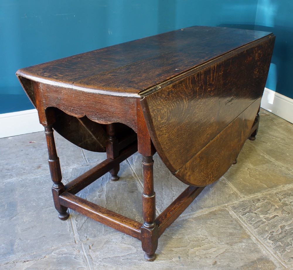 A large 18th-century dark oak gateleg dining table with a circular drop-leaf top supported by turned legs and stretchers. View VII
