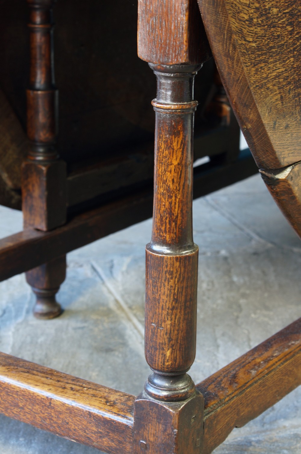 A large 18th-century dark oak gateleg dining table with a circular drop-leaf top supported by turned legs and stretchers. View VIII