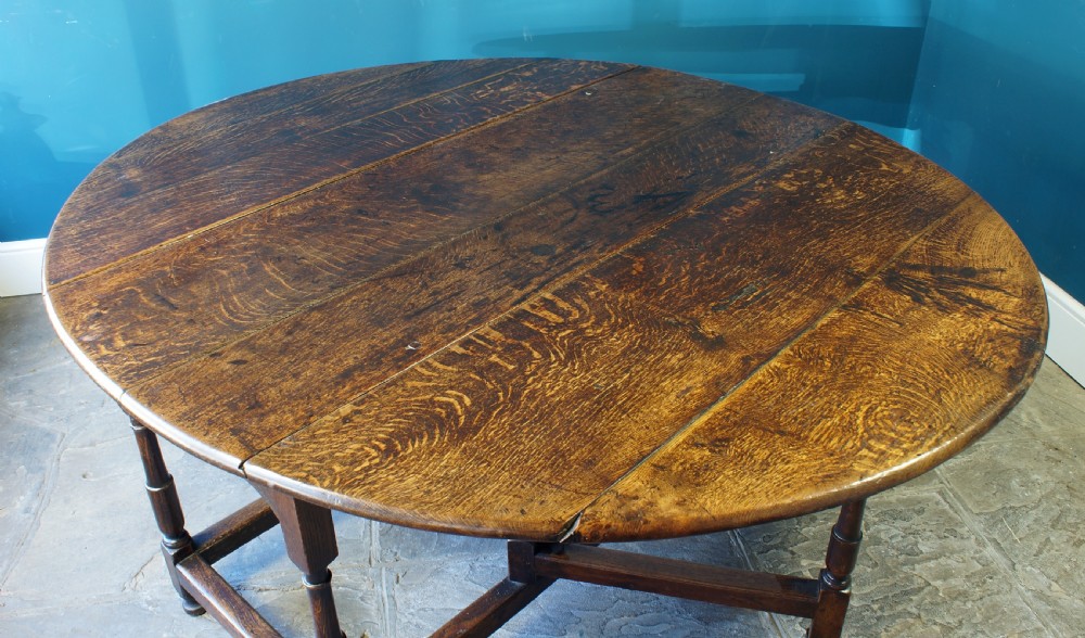 A large 18th-century dark oak gateleg dining table with a circular drop-leaf top supported by turned legs and stretchers.