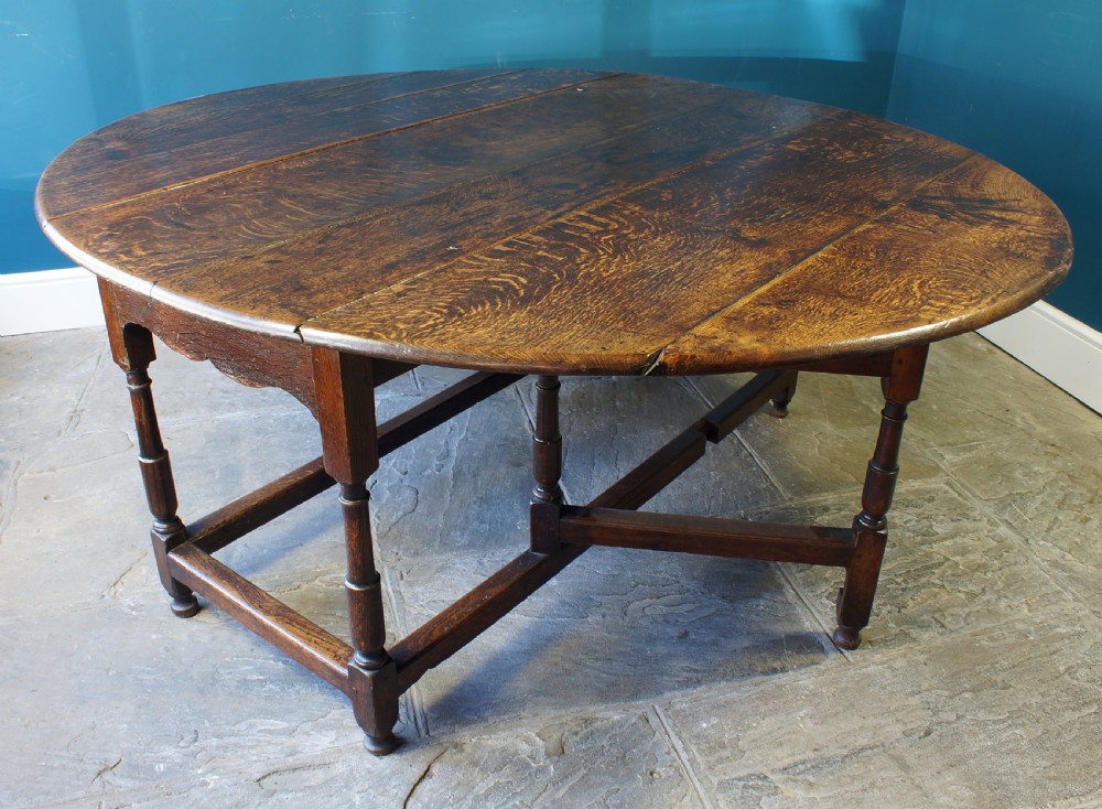 A large 18th-century dark oak gateleg dining table with a circular drop-leaf top supported by turned legs and stretchers. View X