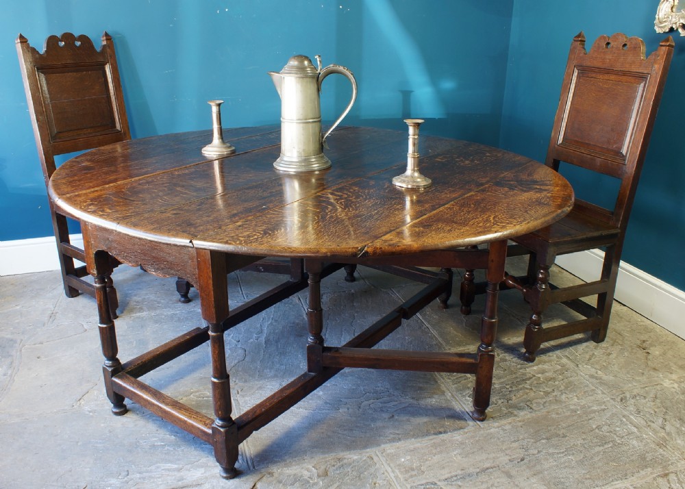 A large 18th-century dark oak gateleg dining table with a circular drop-leaf top supported by turned legs and stretchers. View XI
